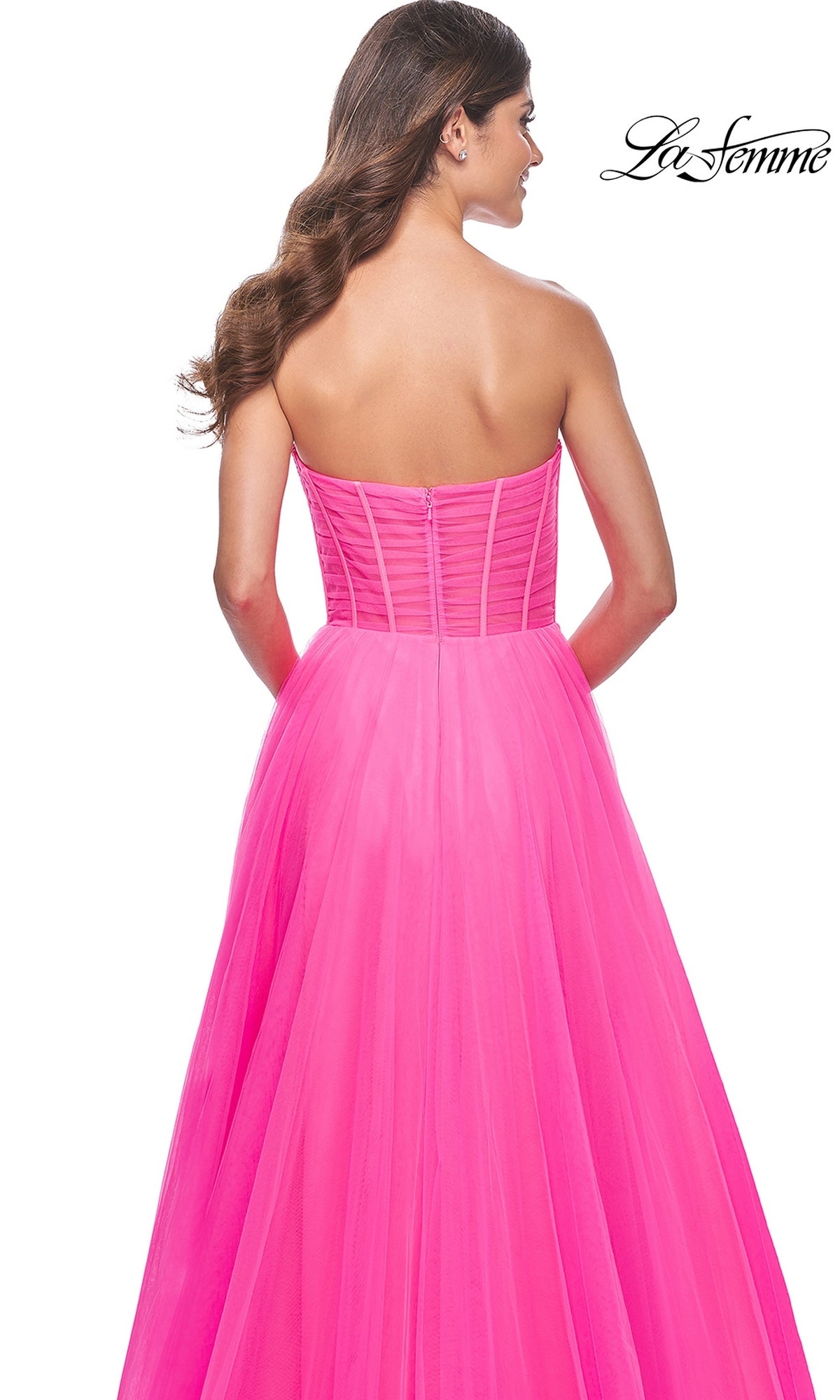 A woman models the La Femme Long Pink Corset A-Line Prom Dress 32341, a strapless neon pink gown with a fitted corset-style bodice and floor-length skirt, shown from the back.